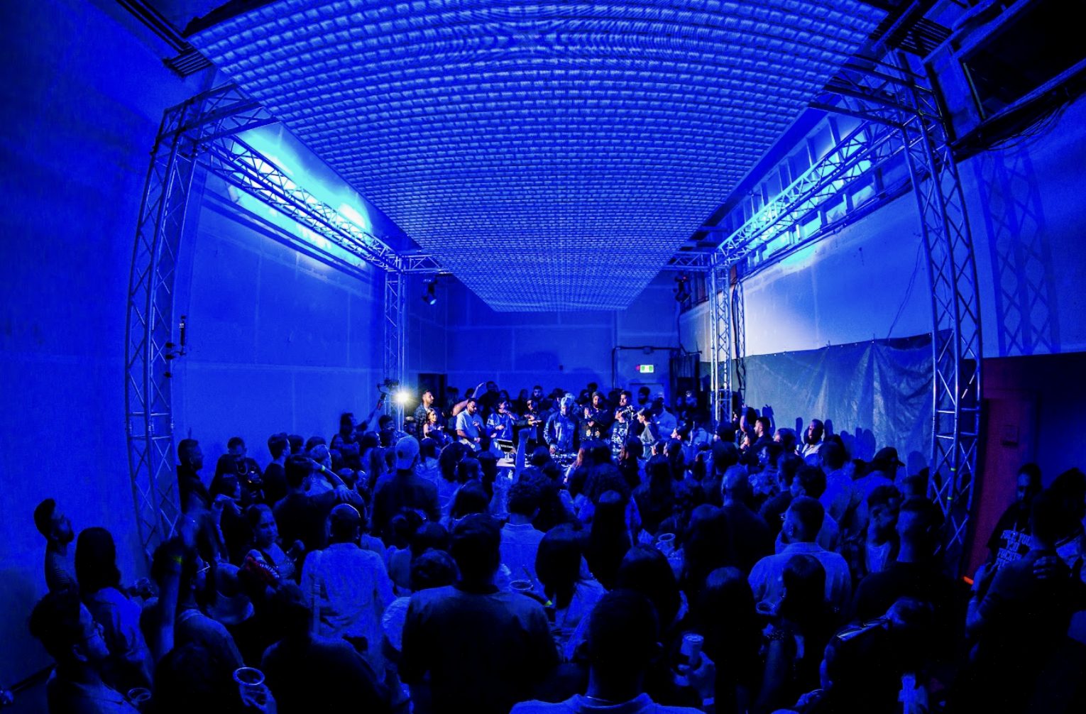 An audience gathered close to the stage under blue projection light