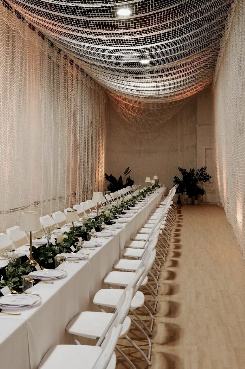 The downstairs space by day, netting draped overhead, a long white banquet table running the length of the room