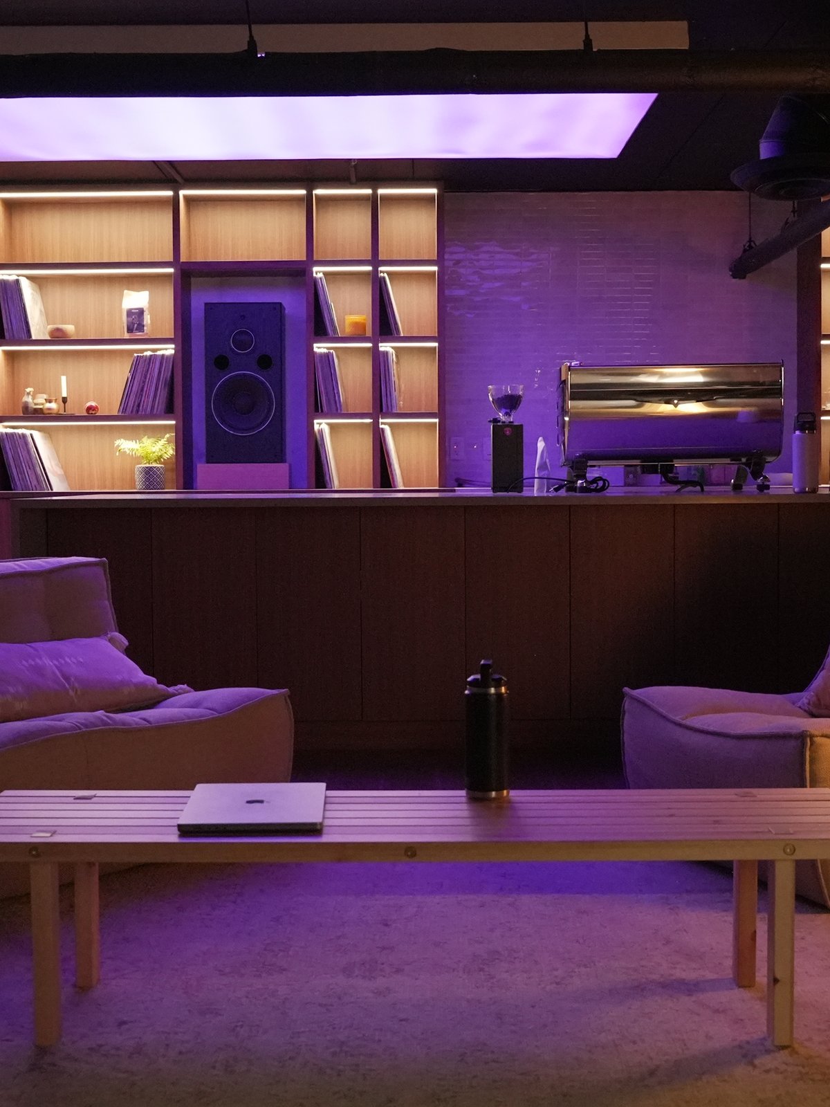 The listening room at night, backlit shelves of records and hi fi speakers behind the coffee bar, with lounge seating